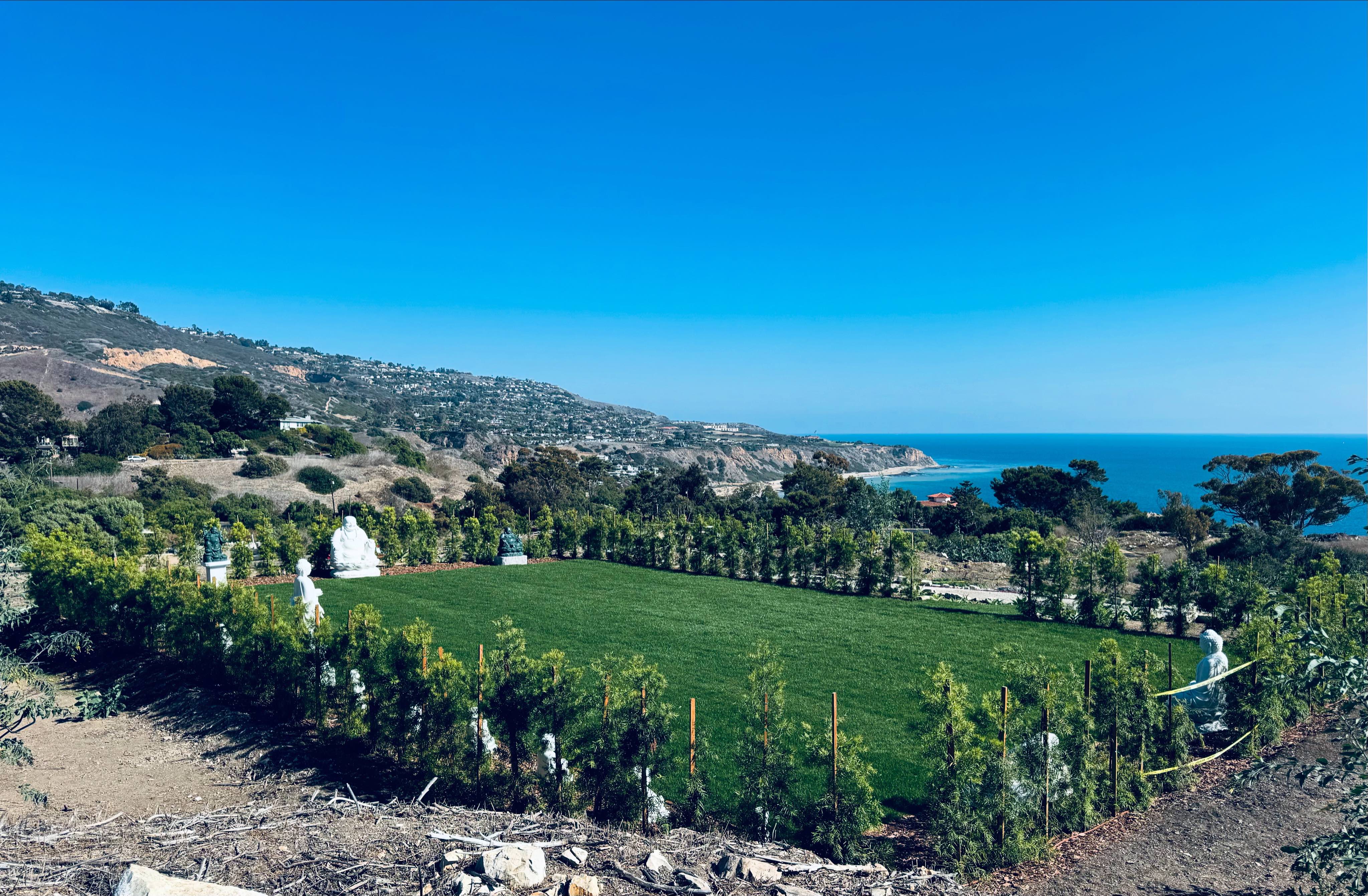 Elevated panoramic view of Plaza Sunshine with pristine green lawn, white Buddha statues, and Palos Verdes coastline