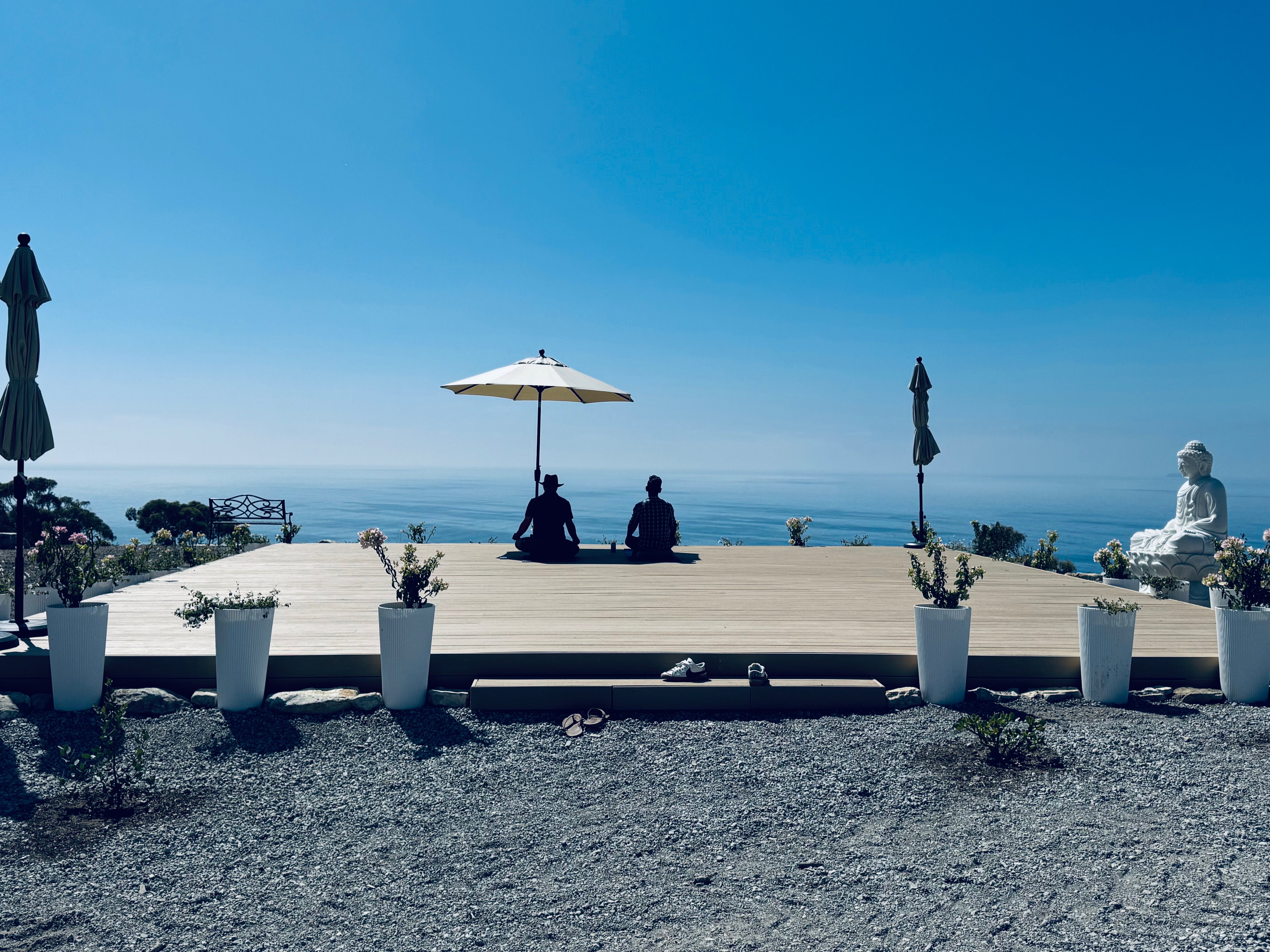 Meditation deck with two people in meditation pose and Buddha statue overlooking Pacific Ocean