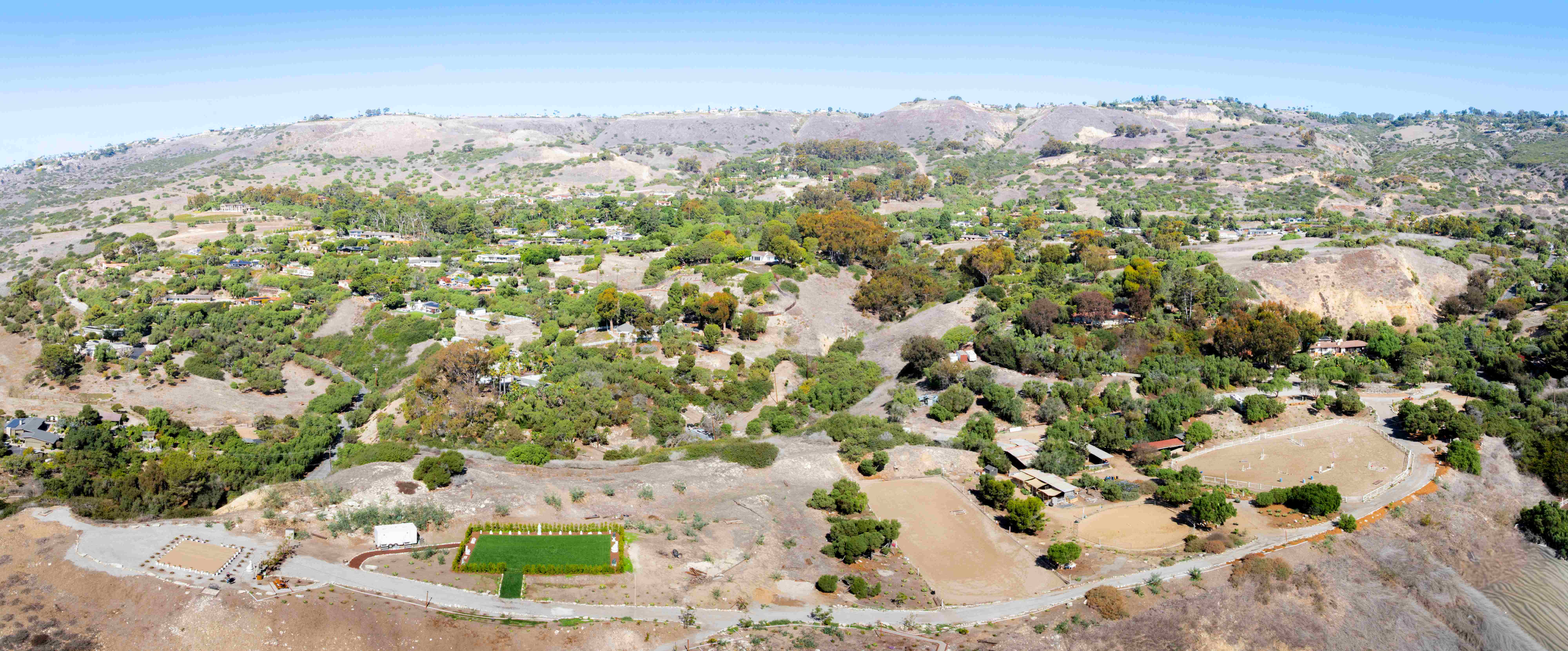 Wide-angle aerial panorama of Infinite Hill property nestled in rolling Palos Verdes hills with equestrian facilities