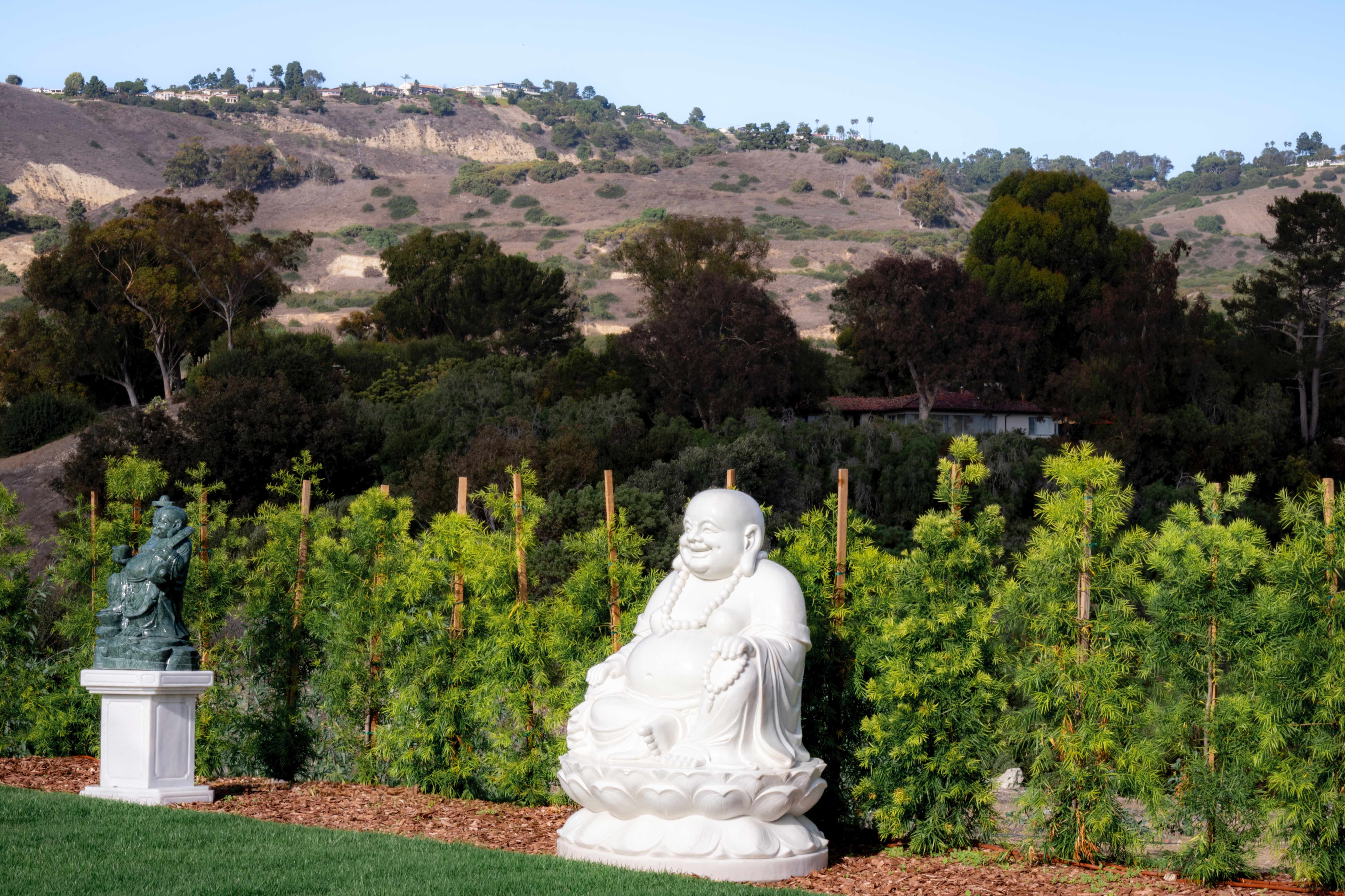 Laughing Buddha statue with dark Buddha figure on pedestal against Palos Verdes hills